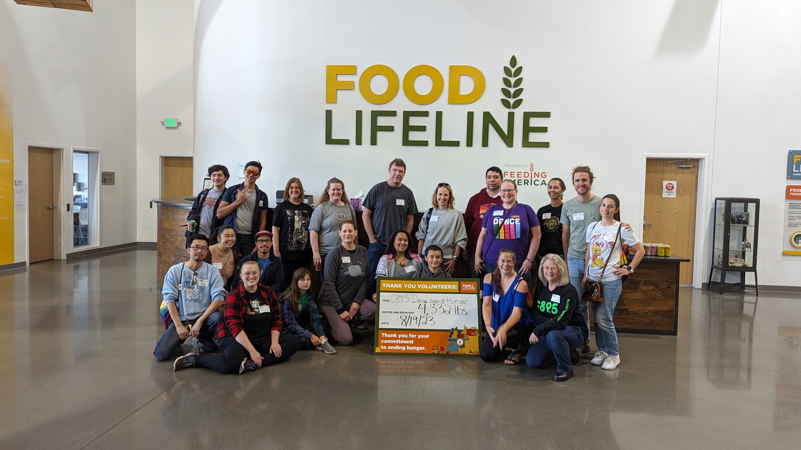 A large group of volunteers standing in front of a sign that says "Food Lifeline" with a smaller sign saying how many tons of food they packed.