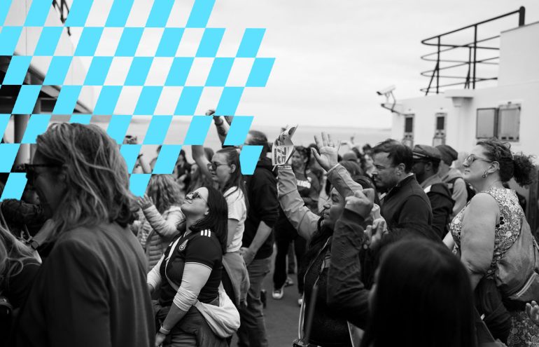 A crowd of people gathers at an outdoor event featuring Bayern Munich. Some individuals are raising their arms, and many appear engaged with the activities. A checkered pattern is overlaid on the left side of the image. The background includes simple buildings and railings, with an overcast sky above.