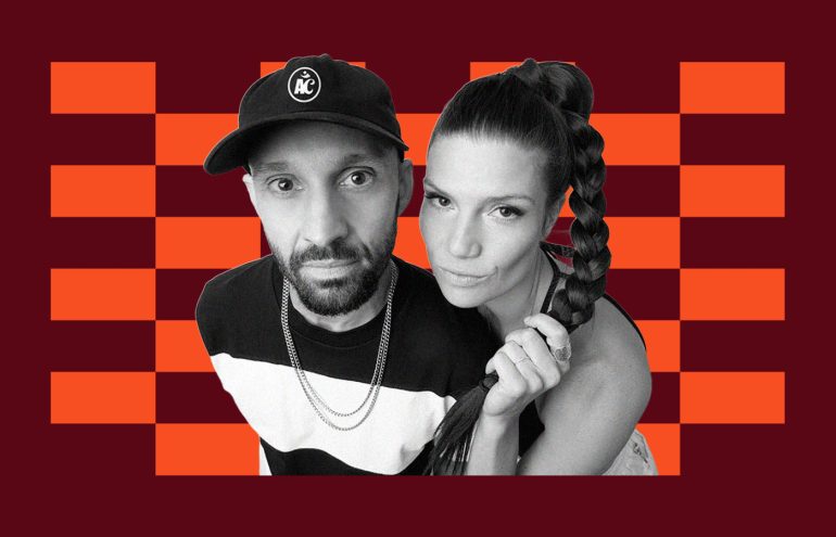 A black and white photo of two people in front of an orange and maroon checkered background. The person on the left wears a cap with an "A" logo. The person on the right has a long braided hairstyle.